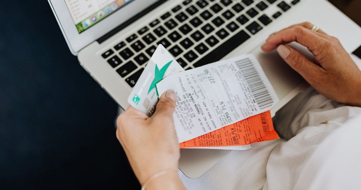 Hands holding a business card and invoices beside a laptop, ready to pay a bill