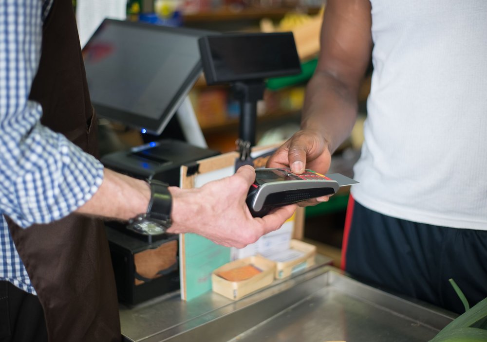 Cashier holding a card terminal as a customer pays by card at a store checkout counter